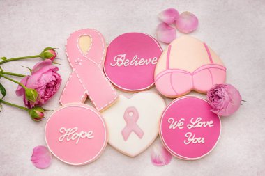 Pembe kurdeleli kurabiyeler ve gri grunge arka planda destekleyici kelimeler. Göğüs kanseri farkındalığı konsepti