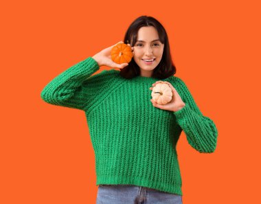 Turuncu arka planda balkabağı olan genç bir kadın.