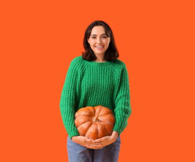 Turuncu arka planda balkabağı olan genç bir kadın.