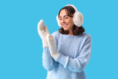 Mavi arka planda, kalın giyinmiş genç bir kadın.