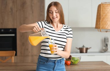 Genç hamile kadın mutfakta cama meyve suyu döküyor.