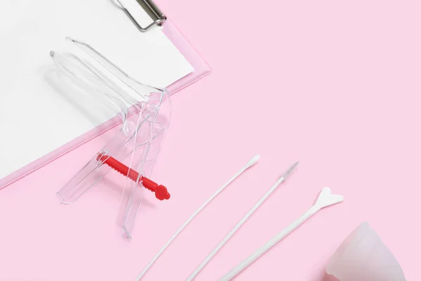 Clipboard with gynecological speculum, menstrual cup and pap smear test tools on pink background