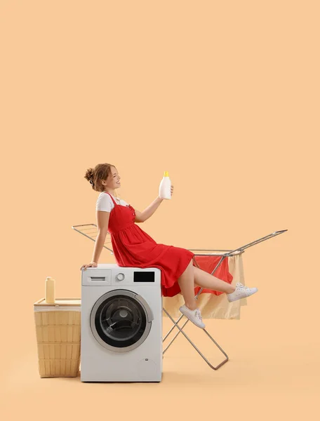 Young woman with laundry detergent and washing machine on beige background