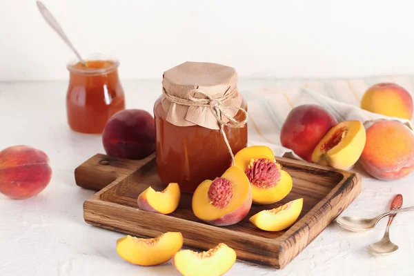 Jar with sweet peach jam and fresh fruits on light background
