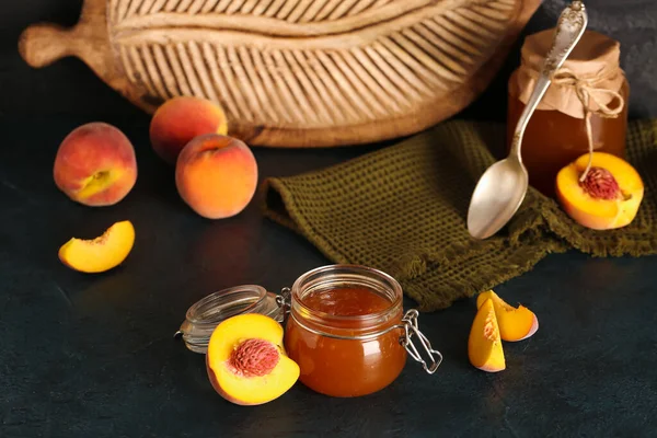 Jar with sweet peach jam and fresh fruits on black background