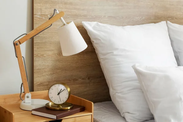 Alarm clock with book and lamp on table in bedroom