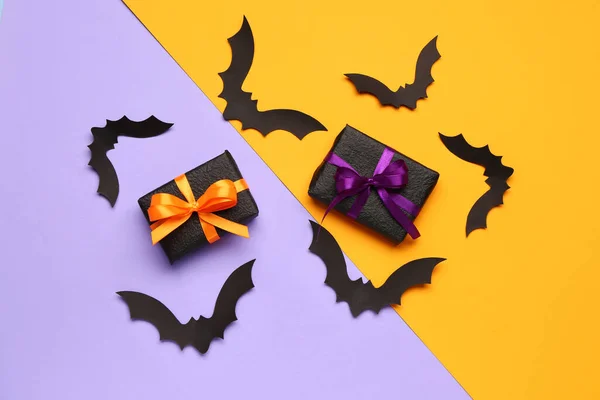 Paper bats for Halloween party and gift boxes on colorful background
