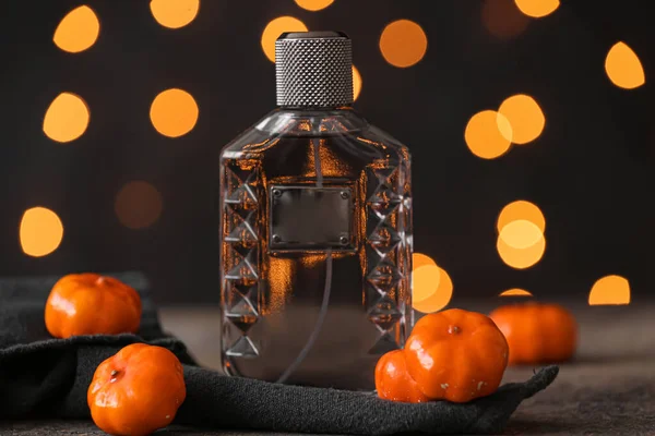 Bottle of elegant perfume with pumpkins for Halloween celebration on grunge table against blurred lights