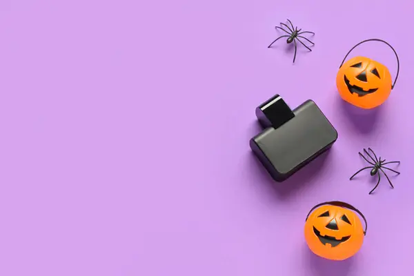 Bottle of elegant perfume with spiders and pumpkins for Halloween celebration on purple background