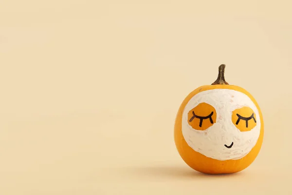 Pumpkin with drawn face and mask on beige background