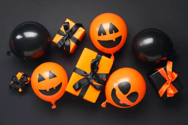 Different funny Halloween balloons and gift boxes on black background