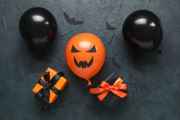 Different funny Halloween balloons with gift boxes and paper bats on dark background