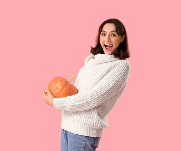 Young woman with pumpkin on pink background