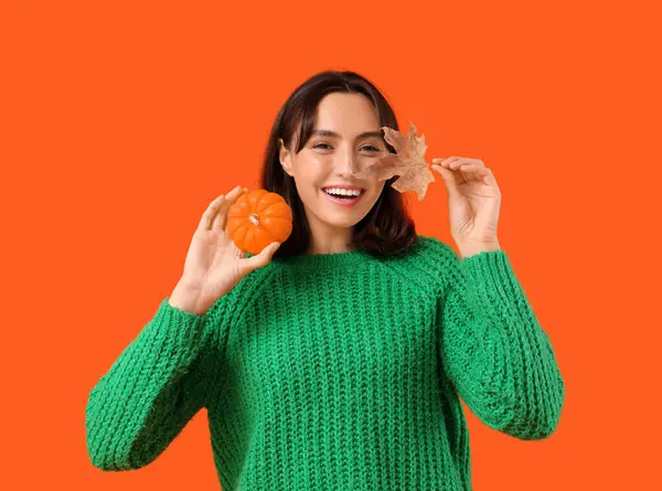 Young woman with pumpkin and autumn leaf on orange background