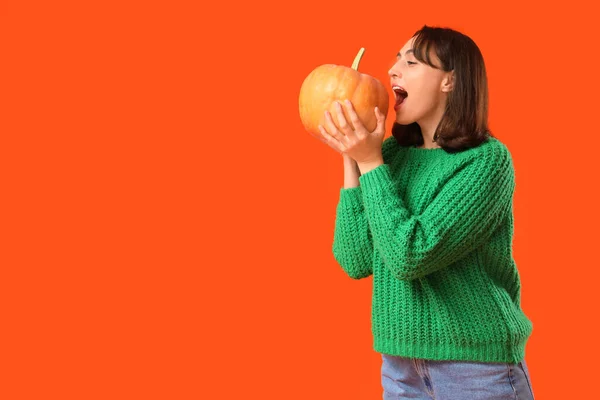 Young woman with pumpkin on orange background