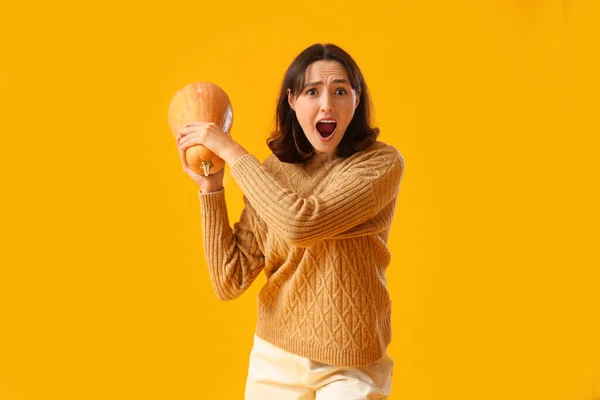 Shocked young woman with pumpkin on yellow background