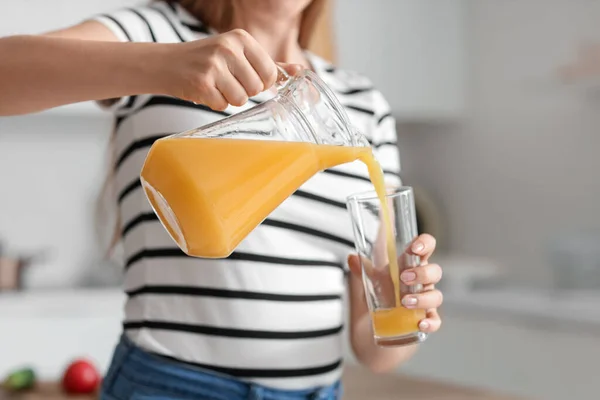Young pregnant woman pouring juice into glass in kitchen, closeup