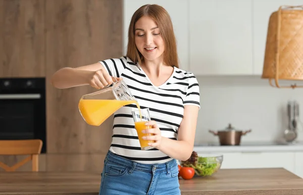 Young pregnant woman pouring juice into glass in kitchen