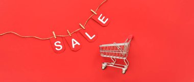 Alışveriş arabası ve kelime satışı kırmızı arka planda.