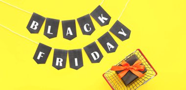 Hediye sepeti ve sarı arka planda siyah cuma yazılı çelenkler.