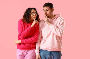 Pembe arka planda sessizlik gösteren genç bir çift.