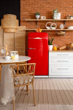 Mutfağın içinde kırmızı buzdolabı, tezgah, raf, masa ve lamba var.