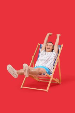 Kırmızı arka planda güvertede oturan mutlu genç adam.