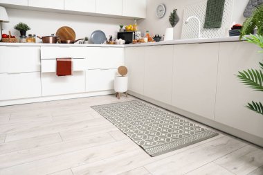 Modern mutfağın içinde şık halı, çöp kutusu ve beyaz tezgahlar var.