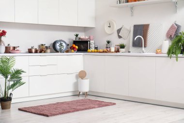 Modern mutfağın içinde şık halı, çöp kutusu ve beyaz tezgahlar var.