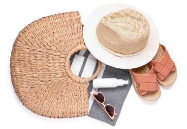 Havalı plaj şapkası, çanta, bir şişe güneş kremi, beyaz arka planda parmak arası terlik ve güneş gözlüğü.