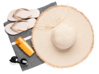 Şık bir plaj şapkası, parmak arası terlik, güneş gözlüğü ve beyaz arka planda bir şişe güneş kremi.