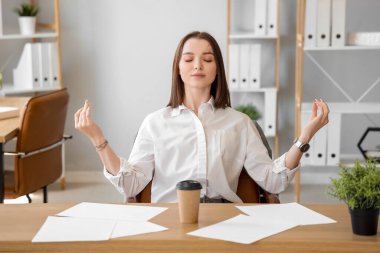 Genç iş kadını ofiste meditasyon yapıyor.