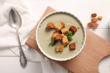 Beyaz ahşap zemin üzerinde kızarmış ekmeklerle bir kase lezzetli krema çorbası.