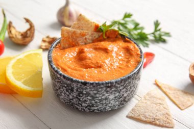 Beyaz ahşap arka planda bir kase limonlu muhammara ve pide.