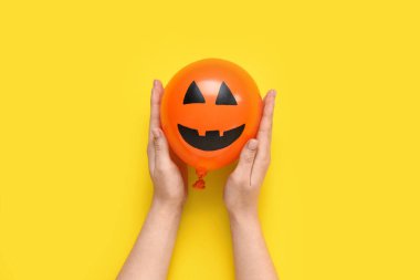 Sarı arka planda komik bir Cadılar Bayramı turuncu balonu olan kadın elleri