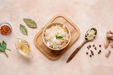 Bir kase lezzetli lahana turşusu ve pembe arka planda baharatlar.