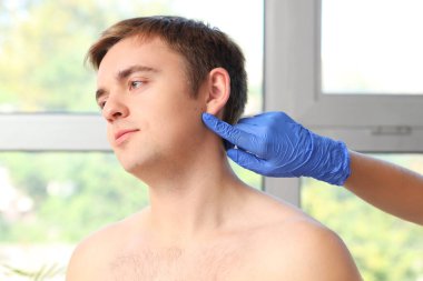 Dermatolog klinikte genç adamın yüzündeki benleri işaret ediyor.