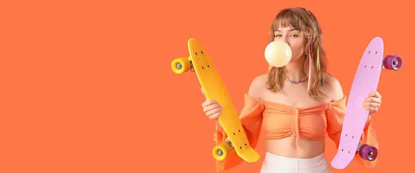 Happy teenage girl with skateboards and chewing gum on orange background with space for text