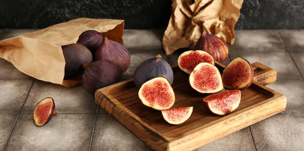 Wooden board and paper bag with fresh ripe figs on table