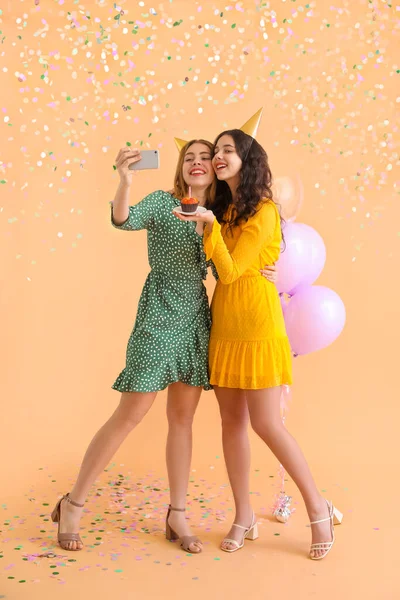 Happy young women with Birthday muffin taking selfie on beige background