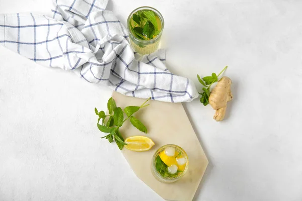 Board with glasses of fresh icy mint tea, lemons and ginger root on white background