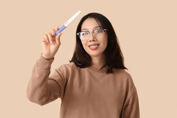 ベージュの背景で妊娠テストを持つ幸せな美しい若いアジアの女性 — ストック写真