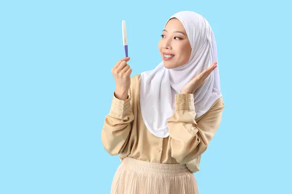 青い背景の妊娠テストでヒジャブで幸せな若いアジアの女性 — ストック写真