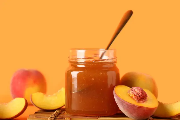 Jar with sweet peach jam and fresh fruits on orange background