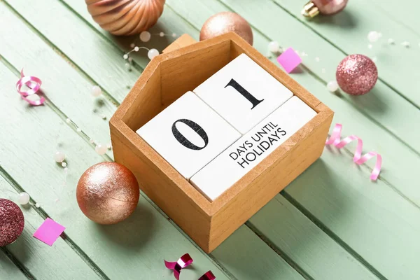 Countdown calendar with Christmas balls and garland on green wooden background