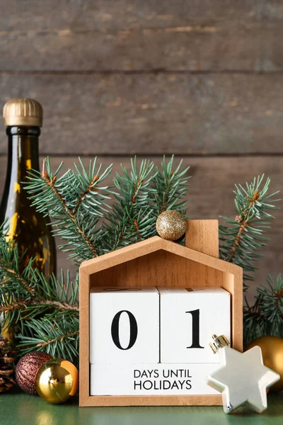 Countdown calendar with Christmas balls, fir branches and bottle of champagne on green wooden table near wall
