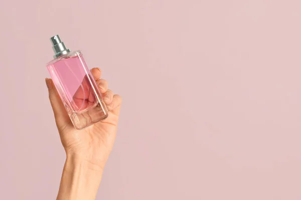 Female hand with bottle of luxury perfume on pink background
