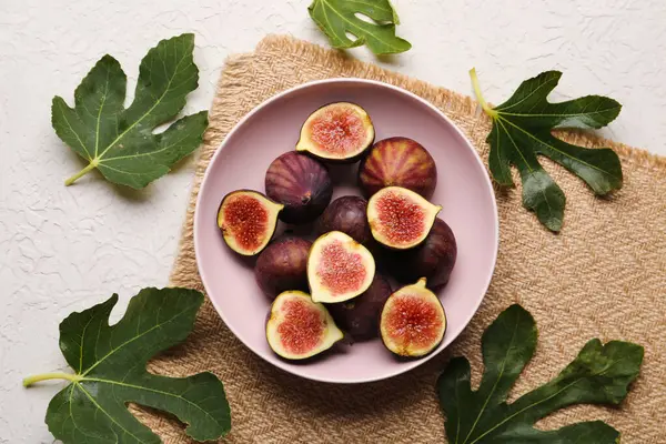 Bowl with fresh ripe figs and leaves on white background