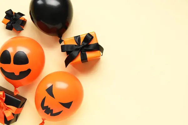 Different funny Halloween balloons and gift boxes on yellow background
