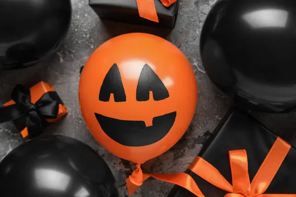 Different funny Halloween balloons and gift boxes on grey background